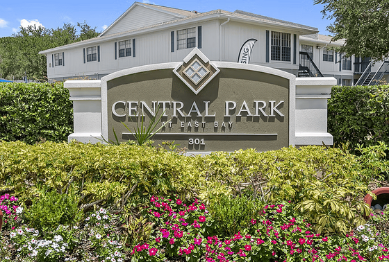 Inviting exterior view of Central Park at East Bay, showcasing beautifully landscaped gardens with vibrant flowers and greenery in front of the welcoming entrance sign.