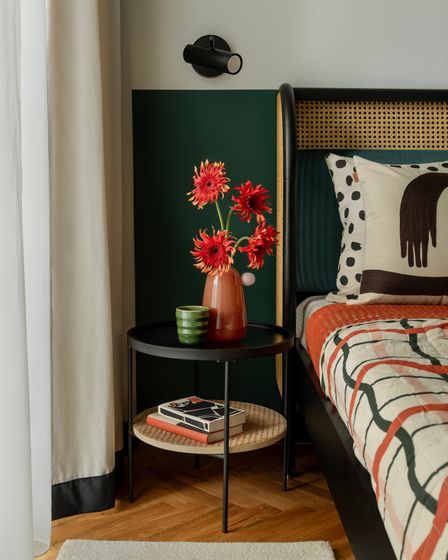 Chic bedroom corner featuring vibrant red flowers in a stylish vase on a modern round table, complemented by a patterned quilt and artistic decor.