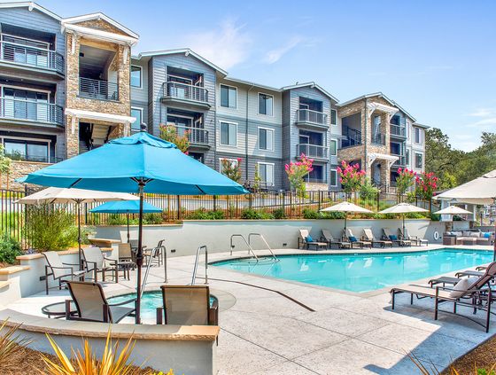 Luxurious apartment complex showcasing a sparkling swimming pool with lounge chairs, vibrant landscaping, and modern architecture.