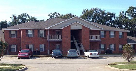 Charming brick apartment building with spacious two-story design, attractive balconies, and convenient parking, nestled in a serene, green neighborhood.