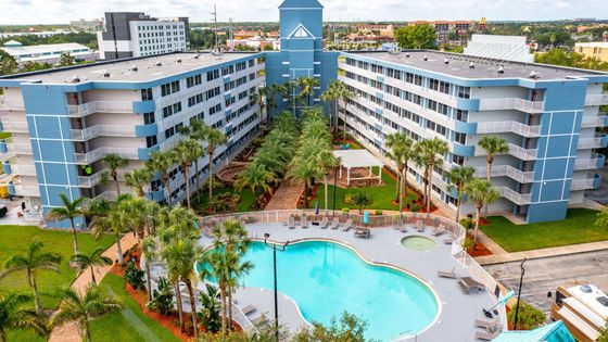 Vibrant residential complex featuring modern blue facades, lush landscaped gardens, and a resort-style swimming pool with lounge chairs.
