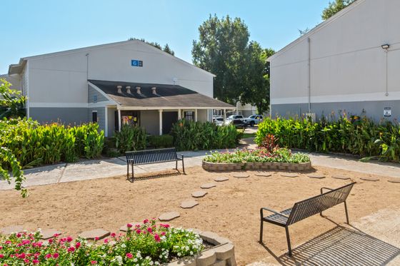 Charming apartment complex with lush garden landscape, vibrant flower beds, and inviting seating area.