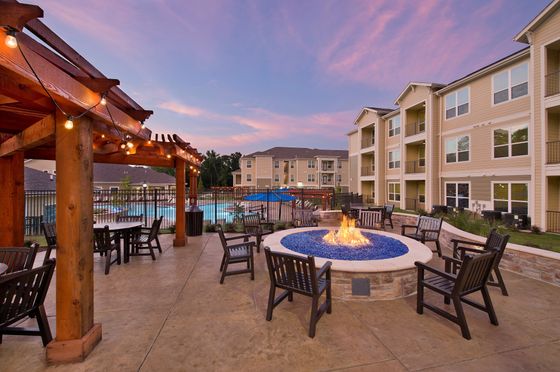 Elegant apartment complex with outdoor seating, illuminated pergola, fire pit, and swimming pool at sunset.