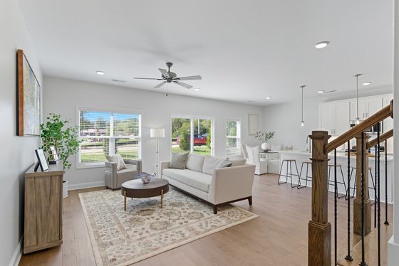 Bright and airy living room with modern furnishings, hardwood floors, and large windows overlooking greenery, seamlessly connected to a stylish kitchen with an open-concept design.