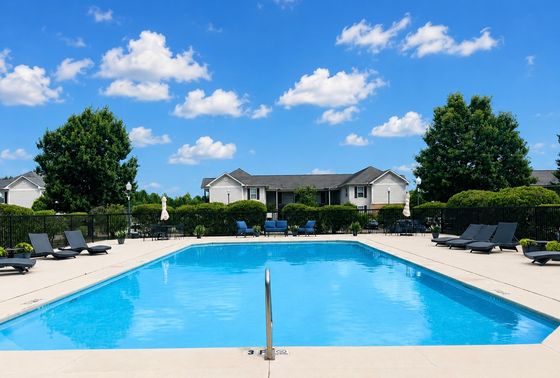 Inviting outdoor pool area with modern lounge chairs, set against a backdrop of beautiful residential homes and lush greenery under a bright blue sky.
