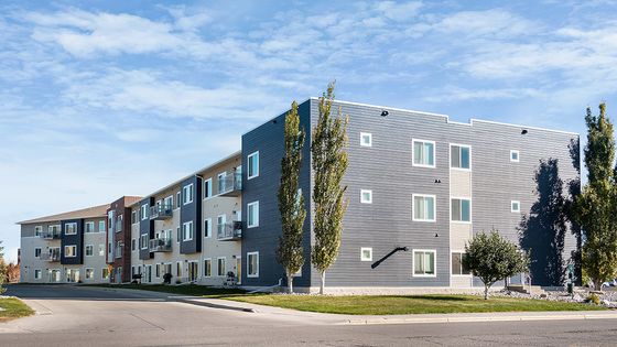 Contemporary three-story apartment building with modern facade and spacious balconies, set against a clear blue sky.