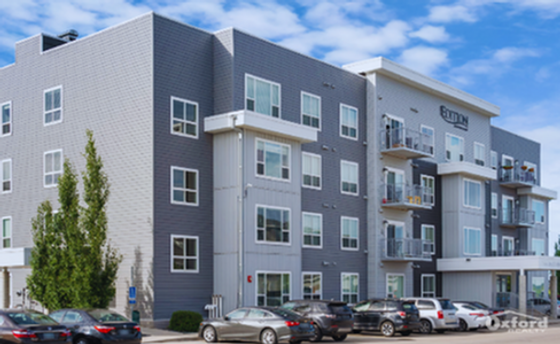 Modern apartment building with sleek architecture, large windows, and ample parking under a bright blue sky.