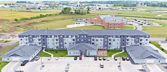 Modern apartment complex with sleek grey facade, surrounded by lush landscape and ample parking options.