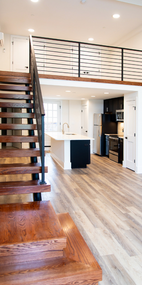 Elegant apartment interior with modern wooden staircase, open-concept kitchen, and stylish loft railing.
