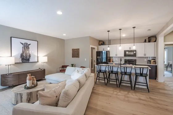 Modern open-concept living room with cozy sectional sofa, stylish horse artwork, and chic kitchen with bar seating.