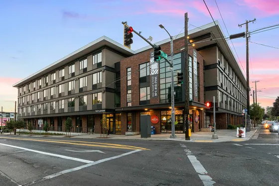 Modern apartment building with sleek architecture located at a bustling street corner during sunset.