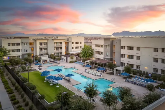 Chic apartment complex with modern architecture, lush landscaping, and inviting swimming pools under a stunning sunset sky.
