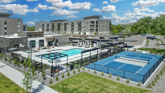 Luxurious apartment complex featuring a pristine pool, modern fitness center, and tennis court set against a backdrop of lush greenery and contemporary architecture.