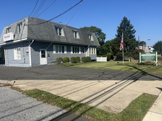 Charming leasing center with classic architecture surrounded by lush greenery and a welcoming American flag.
