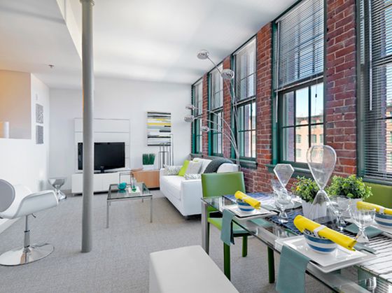 Chic modern living room with brick accent wall, large windows, stylish furniture, and elegant dining setup.
