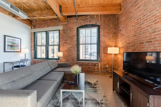 Stylish loft living room with exposed brick walls, modern gray sofa, and large windows.