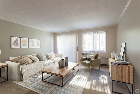 Inviting living room with modern decor, featuring a cozy white sofa, elegant coffee table, and bright natural light from large windows.