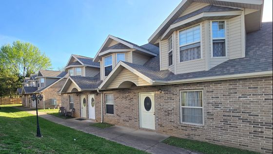 Charming brick townhouses with sloped roofs and large windows, situated in a peaceful neighborhood with lush greenery and well-maintained pathways.