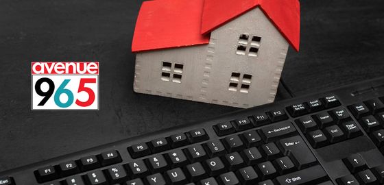 Small house model with red roof next to a computer keyboard on a dark surface, featuring the Avenue 965 logo.
