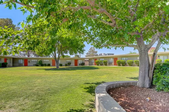 Charming apartment complex with vibrant red doors, nestled within lush green lawns and shaded by mature trees.