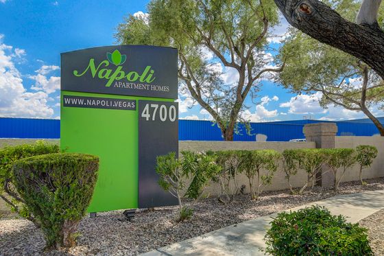 Welcome to Napoli Apartment Homes, showcasing an inviting sign with lush greenery under a vibrant blue sky.