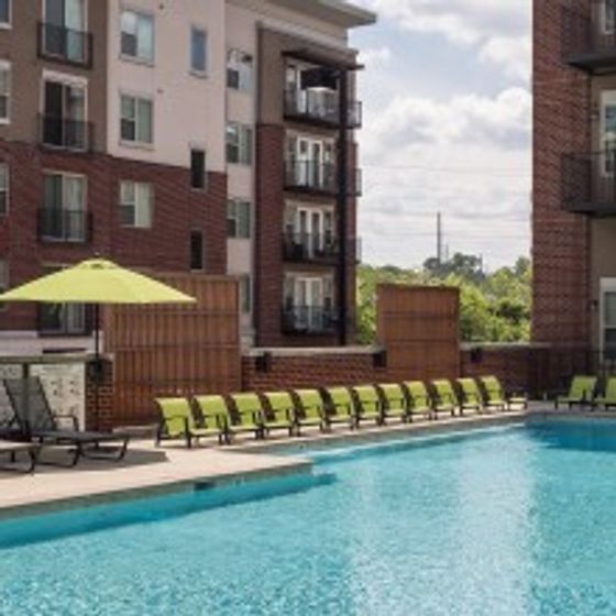 View of Fenced-In Pool Area with Loungers, Seating Areas, and Apartment Building in Background at The Melrose
