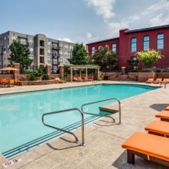 Image of Alpha Mill swimming pool, poolside lounge chairs, cabanas, red brick fence and apartment building exteriors