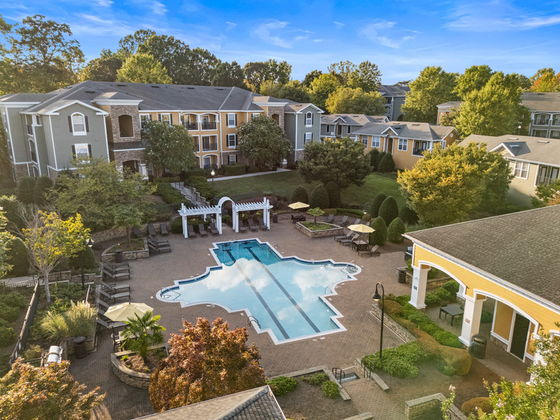 Charming aerial view of a lush apartment community with a uniquely designed swimming pool, surrounded by elegant buildings and vibrant greenery, perfect for serene living at Cottonwood Reserve in Charlotte NC