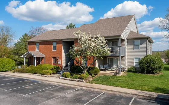 Charming apartment building with a mix of brick and siding, featuring a blooming tree and spacious balconies, surrounded by lush green lawns under a bright blue sky.