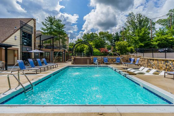 Luxurious outdoor swimming pool with stylish lounge chairs, vibrant greenery, and a modern clubhouse backdrop.