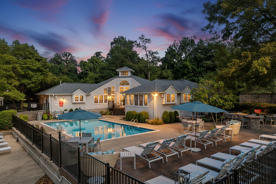 Charming apartment complex with elegant clubhouse, sparkling swimming pool, and lush green surroundings at sunset.
