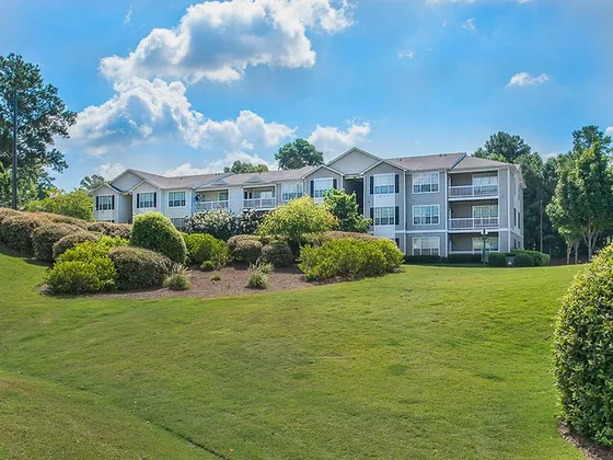 Charming apartment complex with lush landscaping and modern architecture under a bright blue sky.