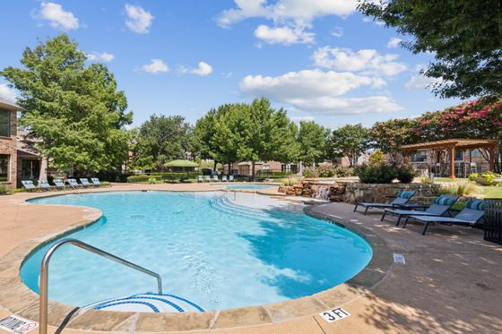 Inviting community pool surrounded by lush greenery, lounge chairs, and a charming pergola under a bright blue sky at Enclave on Golden Triangle.
