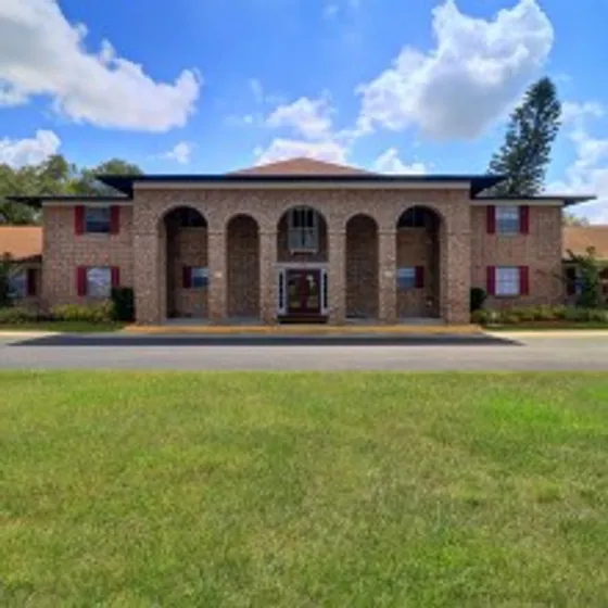 The Rio Apartments, exterior, brick building, high archways, large grass area, driveway, trees, blue skies