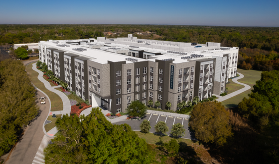Modern apartment complex with sleek design, surrounded by lush greenery and ample parking space, offering a serene residential experience.