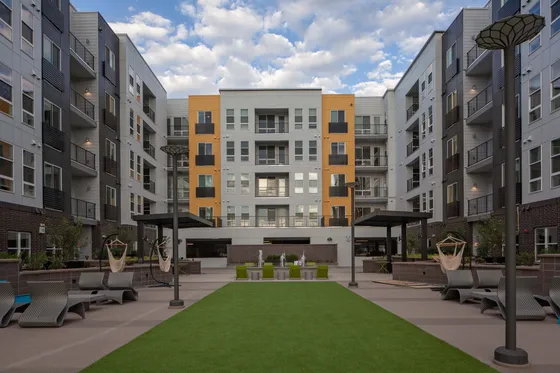 Modern apartment complex with vibrant facade, spacious outdoor courtyard with plush seating, and cozy hammocks.