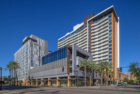 Modern urban apartment building with sleek architectural design, featuring large windows and a vibrant cityscape setting under a clear blue sky.