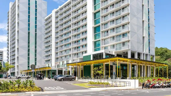 Modern high-rise apartment building with spacious balconies, surrounded by lush greenery and vibrant street scene.