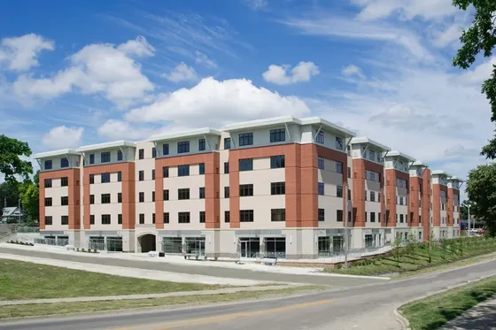 Modern multi-story apartment complex with a striking brick facade, surrounded by lush greenery and a clear blue sky.
