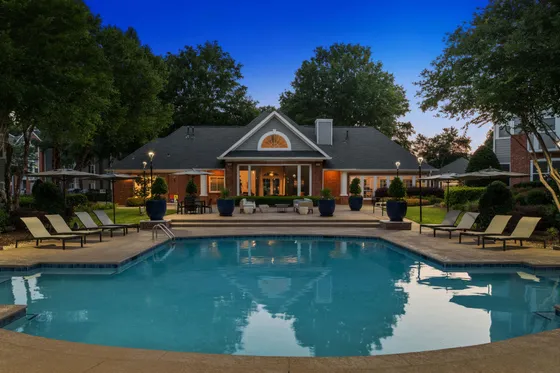 Charming apartment complex with a sparkling pool and cozy clubhouse, surrounded by lush greenery and inviting seating areas, perfect for relaxation and leisure.