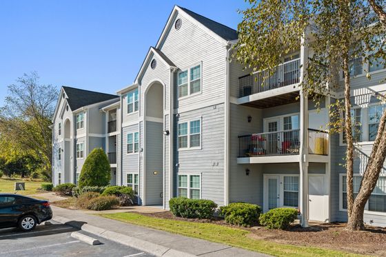 Charming apartment complex with modern architectural design, spacious balconies, and lush green surroundings on a sunny day.