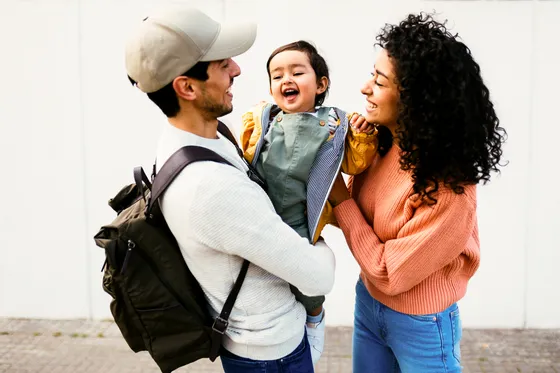 Happy family enjoying a sunny day outdoors, featuring a joyful child in colorful clothing embraced by smiling parents.