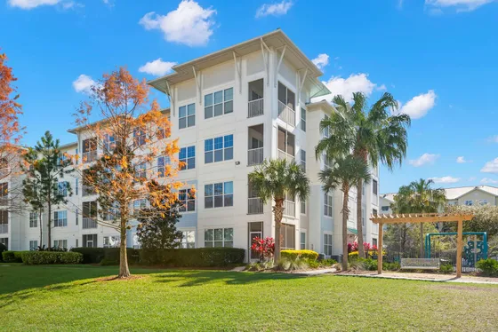 Beautiful modern apartment building surrounded by lush greenery and palm trees, under a clear blue sky.