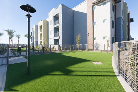 Modern apartment complex with sleek architecture, lush green outdoor area, and palm trees under clear blue skies.