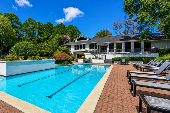 Stunning outdoor pool area with modern lounge chairs, lush greenery, and a charming clubhouse under a clear blue sky.
