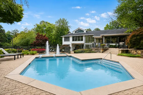 Inviting outdoor pool area with elegant fountains, lush landscaping, and a modern clubhouse backdrop.