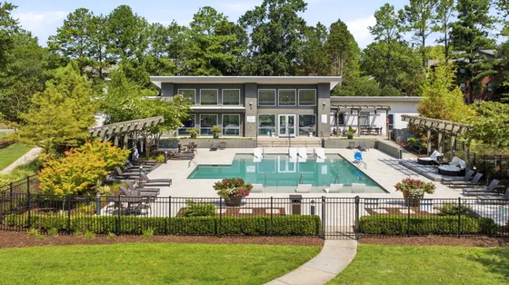 Luxurious apartment complex showcasing a modern clubhouse with a sparkling outdoor pool, surrounded by lush greenery and elegant lounge seating.