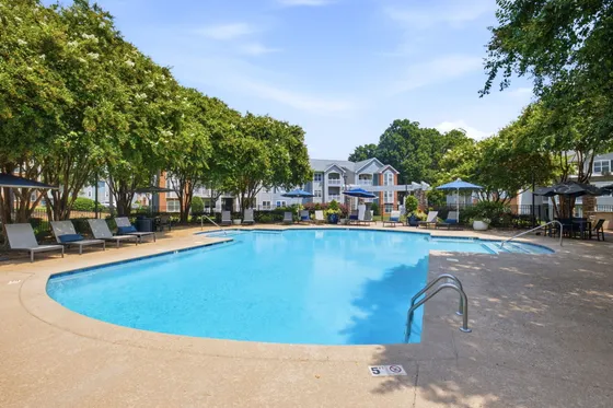 Inviting outdoor pool area surrounded by lush greenery and modern apartment buildings, perfect for relaxation and leisure.