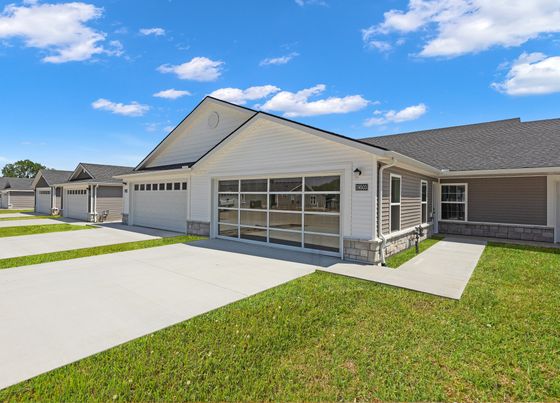 Charming modern duplex with large garage doors and lush green lawns under a clear blue sky.