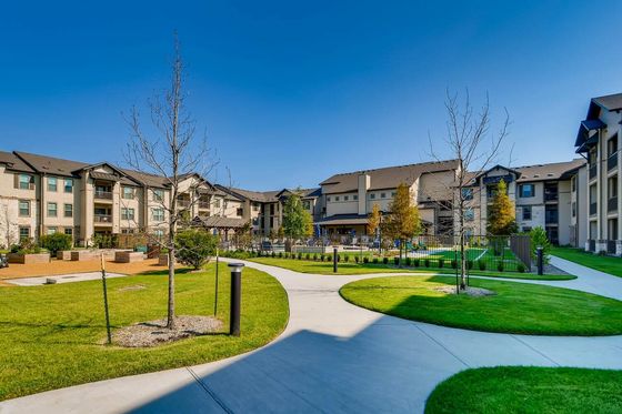 Charming apartment complex with modern architecture, lush green lawns, and inviting walkways under a clear blue sky.
